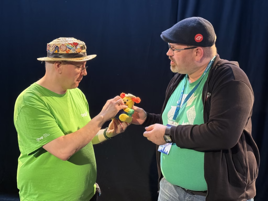 Christoph giving Robert a crocheted personalized Wapuu with green shirt, glasses and straw hat.
